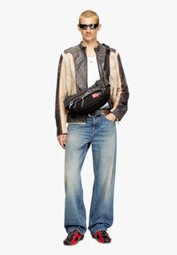 Black leather jacket with a photo print, white tank top, faded blue jeans, and red-accented black sneakers. Black crossbody bag with logo.