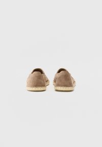 Barna velúr slip-on cipők, texturált felülettel, lekerekített hátsó résszel és világos színű, kontrasztos talpakkal. Az éleken varrás található.