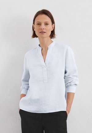 Lichtblauwe linnen blouse met een opstaand kraagje, driekwart mouwen en een voorknopsluiting. Zachte textuur en een losse pasvorm.