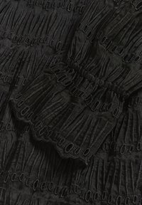Tissu noir avec des lignes brodées verticales et des boucles ovales formant un motif texturé et superposé avec des bords festonnés.