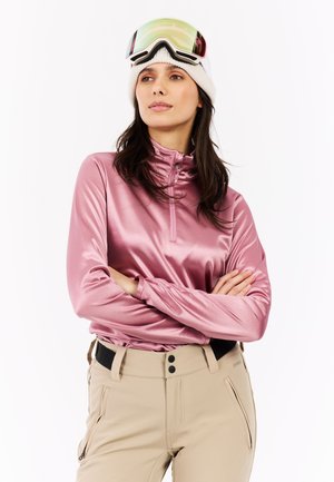 Light pink, long-sleeve, zip-up top with a high collar and smooth texture, paired with beige snow trousers featuring zip pockets and a black waistband.