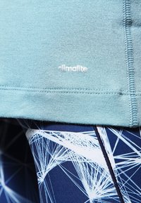 Lysblå sportstrøje lavet af blødt stof, med et hvidt 'climalite' logo. Bæret med mønstrede marineblå leggings, der viser hvide geometriske designs.
