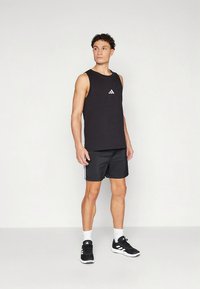 Μαύρο αθλητικό τοπ χωρίς μανίκια με μικρό λευκό λογότυπο, συνδυασμένο με μαύρο σορτς με ρίγες στο πλάι και μαύρα αθλητικά παπούτσια.