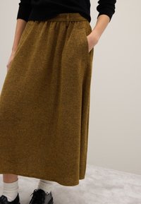 Jupe longue en tissu texturé marron à motif chevrons, dotée d'une taille haute, de poches latérales et d'une silhouette fluide.