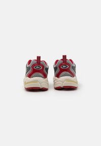 Red and gray athletic shoes with mesh panels, round toe, and textured sole. Features pull tabs and reflective branding on the heel.