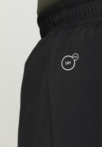 Czarne sportowe spodnie o gładkiej fakturze, z elastycznym pasem i białym logo "DRY CELL" po lewej stronie.