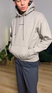 Light grey hoodie with drawstrings, front pocket, and black text reading "PEGADOR." Worn over dark, loose-fitting pants.