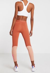 Leggings a vita alta in terracotta e rosa chiaro, realizzati in tessuto elasticizzato. Presentano un design a blocchi di colore con il marchio sul polpaccio.
