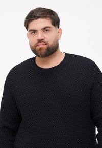 Czarny sweter o teksturowanej powierzchni z geometrycznym wzorem, okrągłym dekoltem i długimi rękawami. Wykonany z miękkiego materiału dzianinowego.