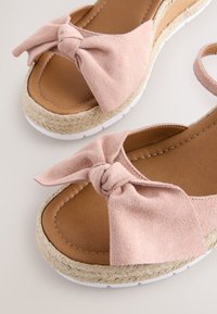 Open teensandalen met lichtroze suède strikjes, lichtbruine gevoerde binnenzolen, gevlochten jute plateauzolen en witte rubberen buitenzolen.