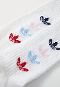 Calze bianche a coste con design di foglie ricamate in rosso, rosa, blu e blu navy. La texture del tessuto è liscia ed elastica.