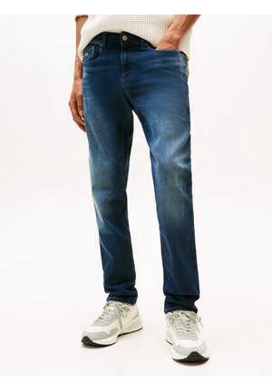 Donkerblauwe denim jeans met een straight leg ontwerp, voorzien van subtiele slijtageplekken, vijf zakken en een klassieke knoopsluiting, gecombineerd met lichte sneakers.