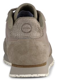 Tanin tenisice s teksturiranim, tkanim uzorkom na peti. Sadrži gornji dio od antilopa, gumeni potplat i okrugli logo na stražnjem dijelu.