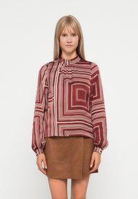 Bordeauxfarbene Bluse mit einem Muster aus horizontalen und vertikalen weißen Streifen, ausgestattet mit einem gerafften hohen Kragen und langen Ärmeln, kombiniert mit einem braunen Rock.