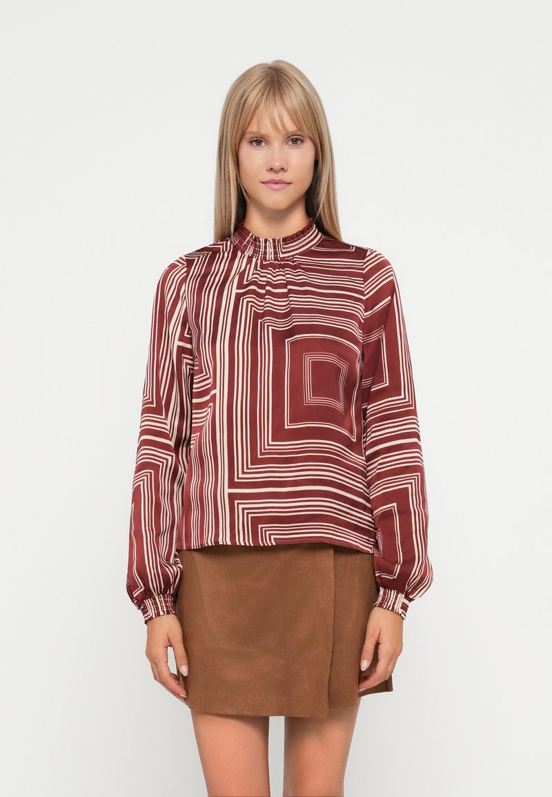 Bordeauxfarbene Bluse mit einem Muster aus horizontalen und vertikalen weißen Streifen, ausgestattet mit einem gerafften hohen Kragen und langen Ärmeln, kombiniert mit einem braunen Rock.