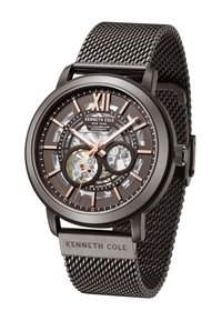 Montre avec bracelet en maille noir, mouvement automatique transparent, accents en bronze et un chiffre XII bien en évidence. Présente un cadran texturé et un logo.