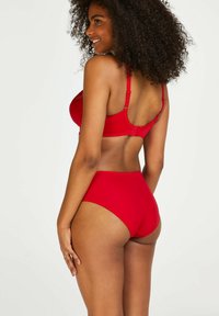 Rode beha en hoge taille bikini onderbroek, beide gemaakt van een gladde stof. De beha heeft verstelbare bandjes en een haaksluiting op de rug.