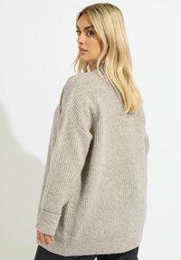 Ljusgrå stickad tröja med en lös passform, ribbad textur och långa ärmar, med rundad halsringning och sprund i fållen.