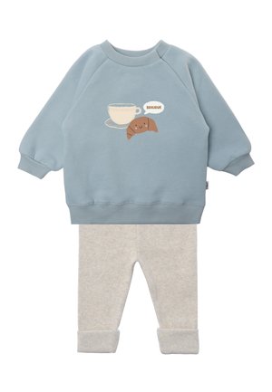 Light blue long-sleeve top with cup and smiling croissant saying "Bonjour," paired with light beige ribbed pants with cuffs.
