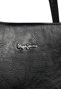 Melnā teksturētā ādas soma sadaļa ar sudraba "Pepe Jeans" logo un redzamu ādas jostas malu augšējā labajā stūrī.