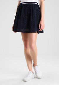 Námořnická modrá sukně ve tvaru A vyrobená z texturované krajkové tkaniny, s elastickým pasem a lemem s malými výřezovými vzory.