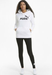 Hanorac alb cu glugă, având logo-ul negru "PUMA", buzunar frontal, asortat cu colanți negri și adidași albi, cu detaliu de logo mic la glezne.