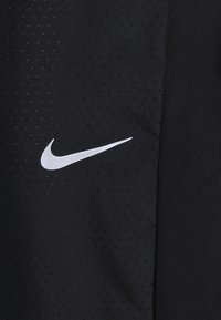 Zwarte sportshirt met een gestructureerde stof met kleine perforaties, verfraaid met een wit Nike-logo aan de linkerzijde.