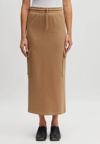 Longue jupe en coton beige avec une taille élastique, un cordon de serrage et des poches latérales. Texture lisse et design simple, idéale pour un style décontracté.