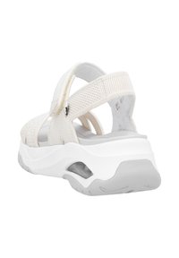 Białe sandały z tkaniny z teksturowanym wierzchem, regulowanymi paskami i grubym białym obcasem. Posiadają amortyzowaną podeszwę i lekkie szare akcenty.
