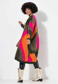 Cardigan en tricot avec des motifs audacieux en vert, rose, orange et marron. Manches longues et coupe décontractée, associé à des bottes métalliques à la cheville.