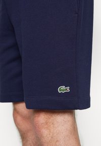 Short bleu marine porté sur une jambe avec un petit logo crocodile vert près de l'ourlet sur le devant.