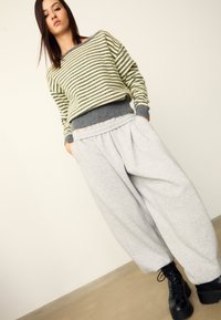 Gestreifter Pullover in Gelb und Grau mit grauem, geripptem Saum, kombiniert mit legeren grauen Jogginghosen und schwarzen Schnürstiefeln.