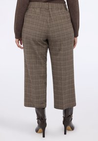 Brązowe w kratkę spodnie o luźnym kroju, z elastycznym paskiem w talii i dwoma tylnymi kieszeniami. W zestawie z czarnymi botkami za kostkę.