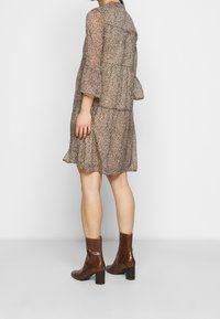 Kevyt, kerroksellinen mekko, jossa on beige pohja ja ruskea leopardikuosi, löysät hihat ja laskostettu helma. Yhdistetty ruskeisiin, paksupohjaisiin boots-kenkiin.