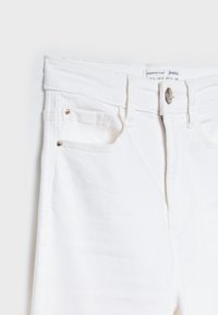 Jean flare raccourcis en denim blanc avec une fermeture à bouton, deux poches avant et de subtils accents en métal doré.