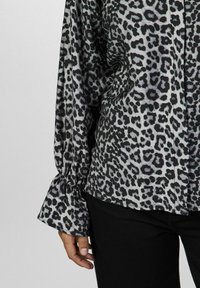 Bluse med leopardprint i grå og sort farveskema, lavet af glat stof med gatherede ærmer og knapdetaljer.
