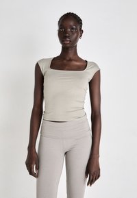 Prijanjeni taupe crop top s kratkim rukavima i kvadratnim izrezom, uparen s visokim svjetlosivim tajicama, glatke teksture, minimalnog dizajna.