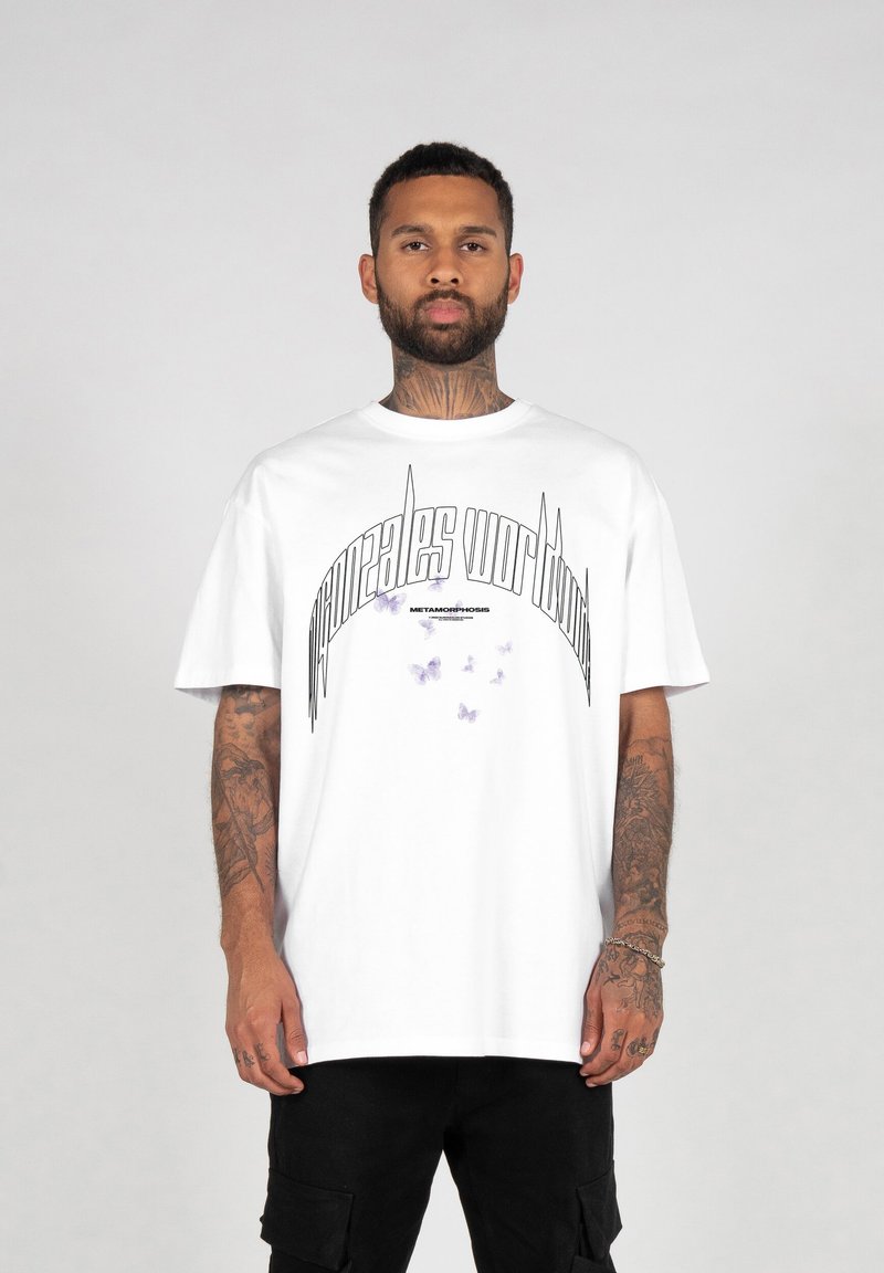 Hvit bomull T-skjorte med en buet grafisk design med teksten "Gonzales World" og lilla sommerfugldetaljer. Korte ermer, løs passform.