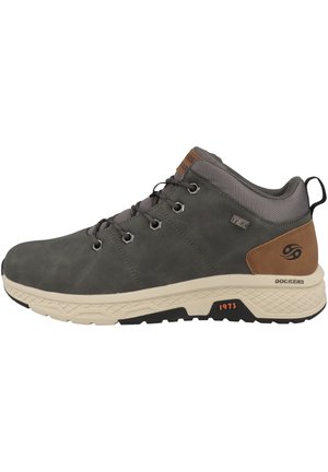 Zapato de senderismo de cuero gris con suela beige clara, punta redonda, cuello de malla texturizada gris y acentos de cuero marrón. Presente los ojetes para los cordones.