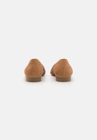 Ballerines en suède marron avec une texture lisse, bout rond, petit talon empilé, et des détails tissés sur les côtés. Design minimaliste sans quincaillerie.