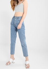 Svart prickig crop top, ljusblå högmidjade jeans och vita klacksandaler. Outfiten har en figursydd design och en avslappnad stil.