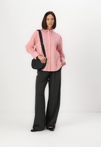 Camicia a righe rossa e bianca abbinata a pantaloni larghi grigi scuri. Borsa a tracolla nera e scarpe basse completano il look.
