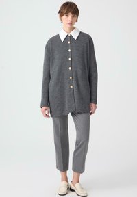 Šedý žebrovaný oversized cardigan s bílým límcem, zdobený zlatými knoflíky. Spárován se šedými plisovanými kalhotami a krémovými mokasíny.