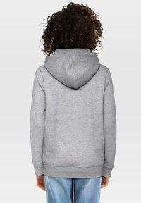 Grå hettegensere med kengurulomme, ribbede mansjetter og kant. Myk tekstur og løs passform, sett fra baksiden. Blå jeans synlige.
