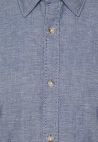 Jasnoniebieska lniana koszula z klasycznym kołnierzykiem, siedmioma guzikami z przodu oraz subtelną teksturą z delikatnym połyskiem.