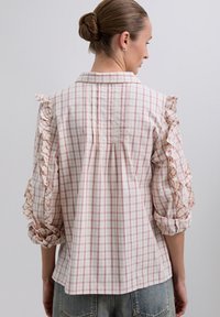 Camisa de cuadros en tela de color rosa claro y blanco, con mangas con volantes, un cuello clásico y un fit relajado con pliegues en la parte trasera.