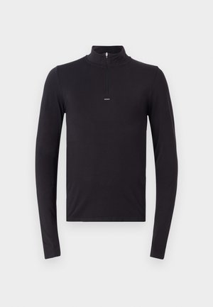 Haut noir à manches longues avec un col zippé quart, présentant une coupe ajustée et des détails de couture minimaux. Le tissu semble lisse et extensible.