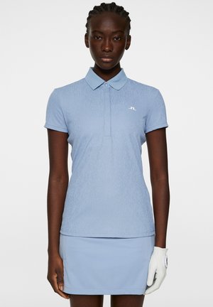 Polo shirt azzurro chiaro con un motivo testurizzato, maniche corte e colletto. Abbinato a una gonna azzurro chiaro coordinata. Dettaglio del logo bianco sul petto.