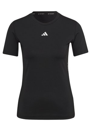 Osoba w czarnym stroju sportowym wykonuje przysiad, trzymając oburącz srebrną hantlę.