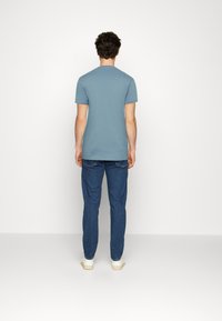 Light blue cotton T-shirt with a crew neck and short sleeves, paired with dark blue denim jeans. View from the back.